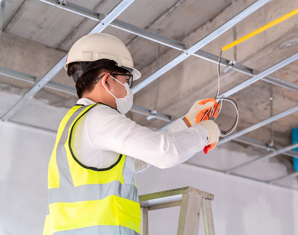 Electrician wearing a mask installing laying electrical cables on the ceiling